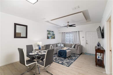 Dining space with a tray ceiling, visible vents, ceiling fan, and light wood finished floors