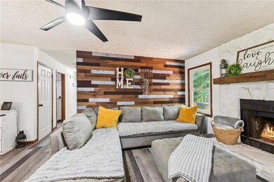 Living area with a textured ceiling, a stone fireplace, ceiling fan, wood finished floors, and wooden walls