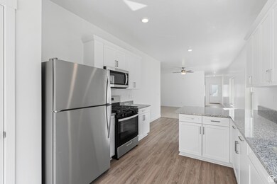 Kitchen with stainless steel appliances, a peninsula, light stone countertops, white cabinetry, and light wood-type flooring