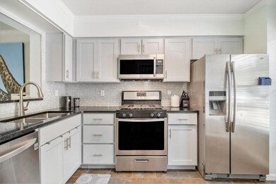 The renovated, modern kitchen features light grey cabinets, black-flecked granite countertops, sparkling icy wall tile, stainless steel appliances, pantry, and washer/dryer space.
