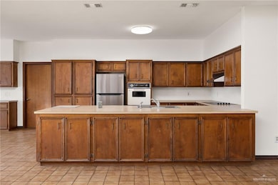 Kitchen with freestanding refrigerator, light countertops, oven, brown cabinetry, and light tile patterned flooring