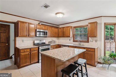 Kitchen featuring appliances with stainless steel finishes, a sink, brown cabinetry, tasteful backsplash, and a breakfast bar
