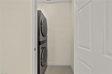 Washroom with stacked washing maching and dryer and light tile patterned flooring
