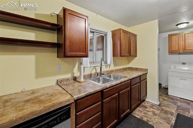 Kitchen featuring washer / dryer, dishwashing machine, open shelves, light countertops, and stone finish flooring