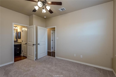 Unfurnished bedroom featuring dark colored carpet, visible vents, ensuite bath, and baseboards