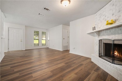 Unfurnished living room with a brick fireplace, dark wood-style floors, and a textured ceiling