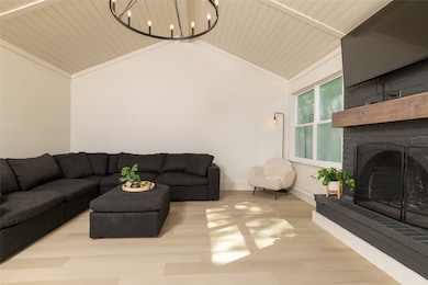 Living room featuring a fireplace, wood finished floors, lofted ceiling, and a chandelier
