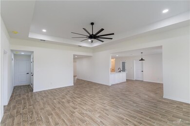 Unfurnished living room with light wood-style flooring, ceiling fan, a raised ceiling, and recessed lighting