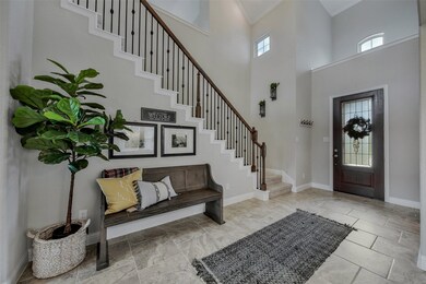 Inviting, light and bright two story foyer with brick-laid tile flooring, crown molding, and wrought iron staircase. Sherwin Williams Agreeable Gray wall color throughout.