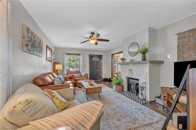 Living room with a fireplace, dark wood-type flooring, and ceiling fan