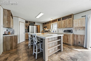 Kitchen featuring open shelves, appliances with stainless steel finishes, a kitchen island, stone tile floors, and light countertops