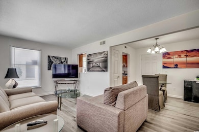 Living area with a chandelier, wood finished floors, a textured ceiling, and baseboards