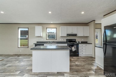 Kitchen featuring black appliances, under cabinet range hood, a kitchen island, dark countertops, and wood finished floors