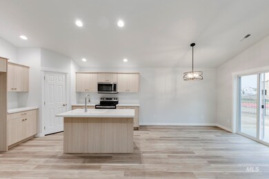 Kitchen with light brown cabinets, decorative light fixtures, appliances with stainless steel finishes, light wood-type flooring, and an island with sink
