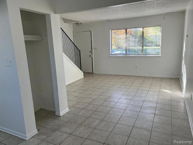 Unfurnished living room featuring light tile patterned floors, a textured ceiling, and stairway