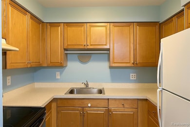 Kitchen with freestanding refrigerator, electric range, brown cabinets, range hood, and light countertops