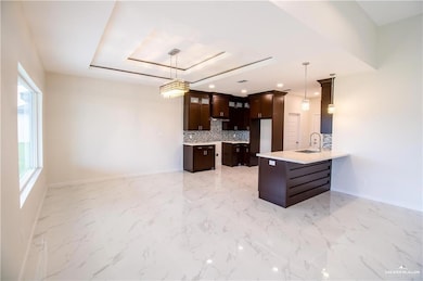 Kitchen with dark brown cabinets, a raised ceiling, tasteful backsplash, hanging light fixtures, and glass insert cabinets
