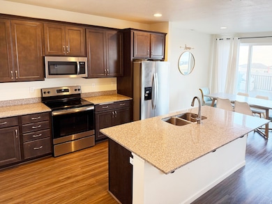 Kitchen featuring stainless steel appliances, dark brown cabinetry, light stone countertops, dark wood-style floors, and recessed lighting