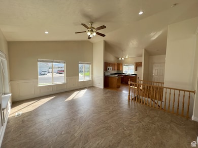 Living room with a decorative wall, a ceiling fan, a wainscoted wall, a chandelier, and lofted ceiling