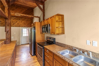 Kitchen with stainless steel appliances, light wood finished floors, brown cabinets, open shelves, and high vaulted ceiling