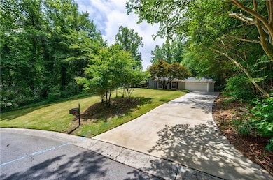 View of property hidden behind natural elements featuring a front lawn, an attached garage, and concrete driveway