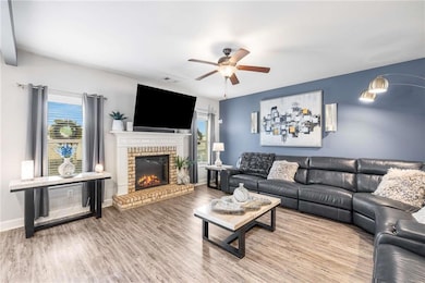 Living area with wood finished floors, a brick fireplace, and a ceiling fan