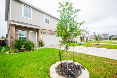 This is a modern two-story home with a brick and siding exterior, featuring an attached two-car garage. The property includes a neatly manicured lawn and a young tree in the front yard, situated in a residential neighborhood with similar homes.