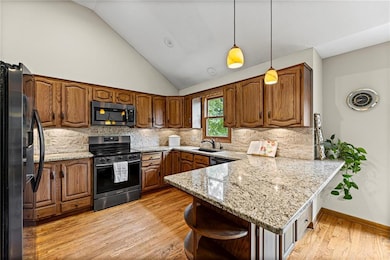 Kitchen with a peninsula, appliances with stainless steel finishes, backsplash, light stone countertops, and high vaulted ceiling
