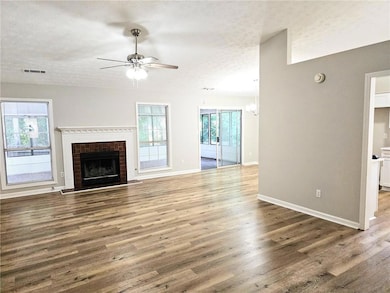 Unfurnished living room with a fireplace, ceiling fan with notable chandelier, a textured ceiling, and hardwood / wood-style floors