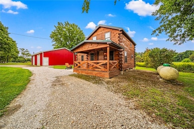 Cabin featuring log siding, an outbuilding, a garage, a pole building, and gravel driveway