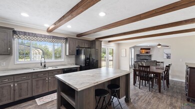 Kitchen with black appliances, beam ceiling, a kitchen bar, dark wood-style flooring, and a fireplace