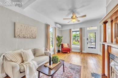 Living room with a wall mounted air conditioner, light wood finished floors, and a ceiling fan