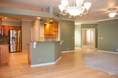 Kitchen featuring decorative backsplash, ornamental molding, stainless steel fridge, light stone counters, and a chandelier