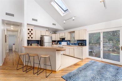 Kitchen with cream cabinetry, high vaulted ceiling, a breakfast bar area, white appliances, and light wood-type flooring