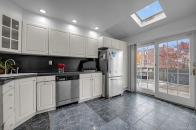 Kitchen with white cabinets, appliances with stainless steel finishes, dark countertops, lofted ceiling, and a skylight