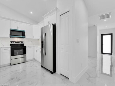 Kitchen with appliances with stainless steel finishes, light marble finish floors, lofted ceiling, white cabinets, and recessed lighting