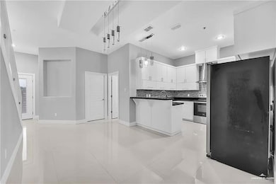 Kitchen featuring stainless steel appliances, light tile patterned floors, white cabinetry, a peninsula, and decorative backsplash