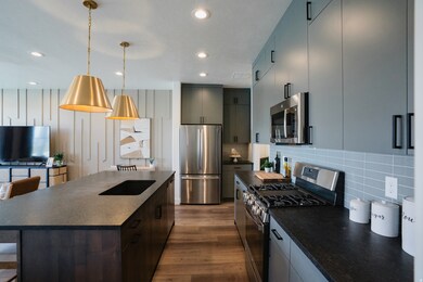 Kitchen featuring dark countertops, appliances with stainless steel finishes, an island with sink, a kitchen breakfast bar, and recessed lighting