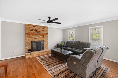 Living room with a brick fireplace, wood-type flooring, ceiling fan, and ornamental molding