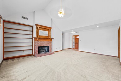 Unfurnished great room with high vaulted ceiling, carpet flooring, and a brick fireplace.