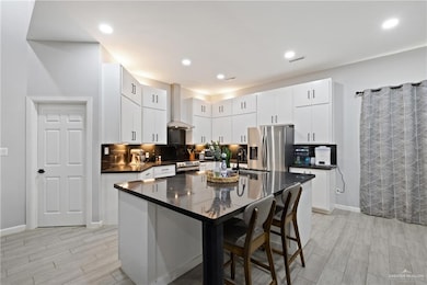 Kitchen featuring tasteful backsplash, a kitchen island with sink, a kitchen bar, wood finish floors, and recessed lighting