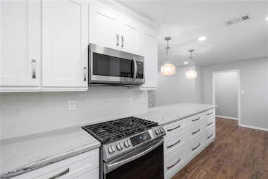 Kitchen with appliances with stainless steel finishes, white cabinets, light stone countertops, recessed lighting, and dark wood-type flooring