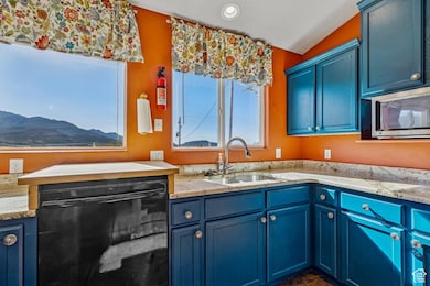 Kitchen with blue cabinets, dishwasher, light stone countertops, and stainless steel microwave