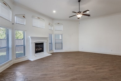 Unfurnished living room with crown molding, dark wood finished floors, a glass covered fireplace, a ceiling fan, and a high ceiling