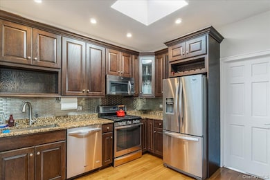 Kitchen with open shelves, dark brown cabinets, appliances with stainless steel finishes, light wood-style floors, and light stone counters