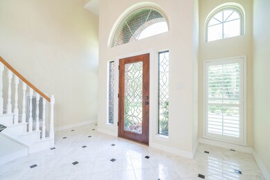 A charming covered front porch leads to this breathtaking leaded glass front door flanked by ornately detailed windows, into a grand foyer with gleaming white tile floors, a soaring two story ceiling, and a sweeping curved staircase.