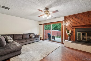 Living area featuring wood finished floors, a glass covered fireplace, ceiling fan, and a textured ceiling