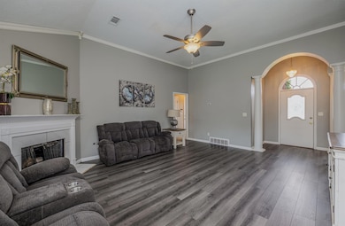 Living area featuring arched walkways, decorative columns, a ceiling fan, dark wood-style flooring, and a tiled fireplace