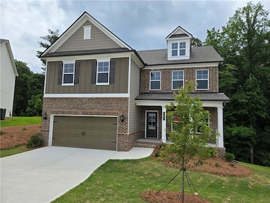 View of front of home with an attached garage, brick siding, concrete driveway, board and batten siding, and a front lawn