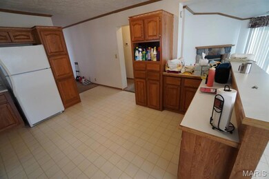 Kitchen with ornamental molding, light countertops, freestanding refrigerator, a textured ceiling, and brown cabinetry